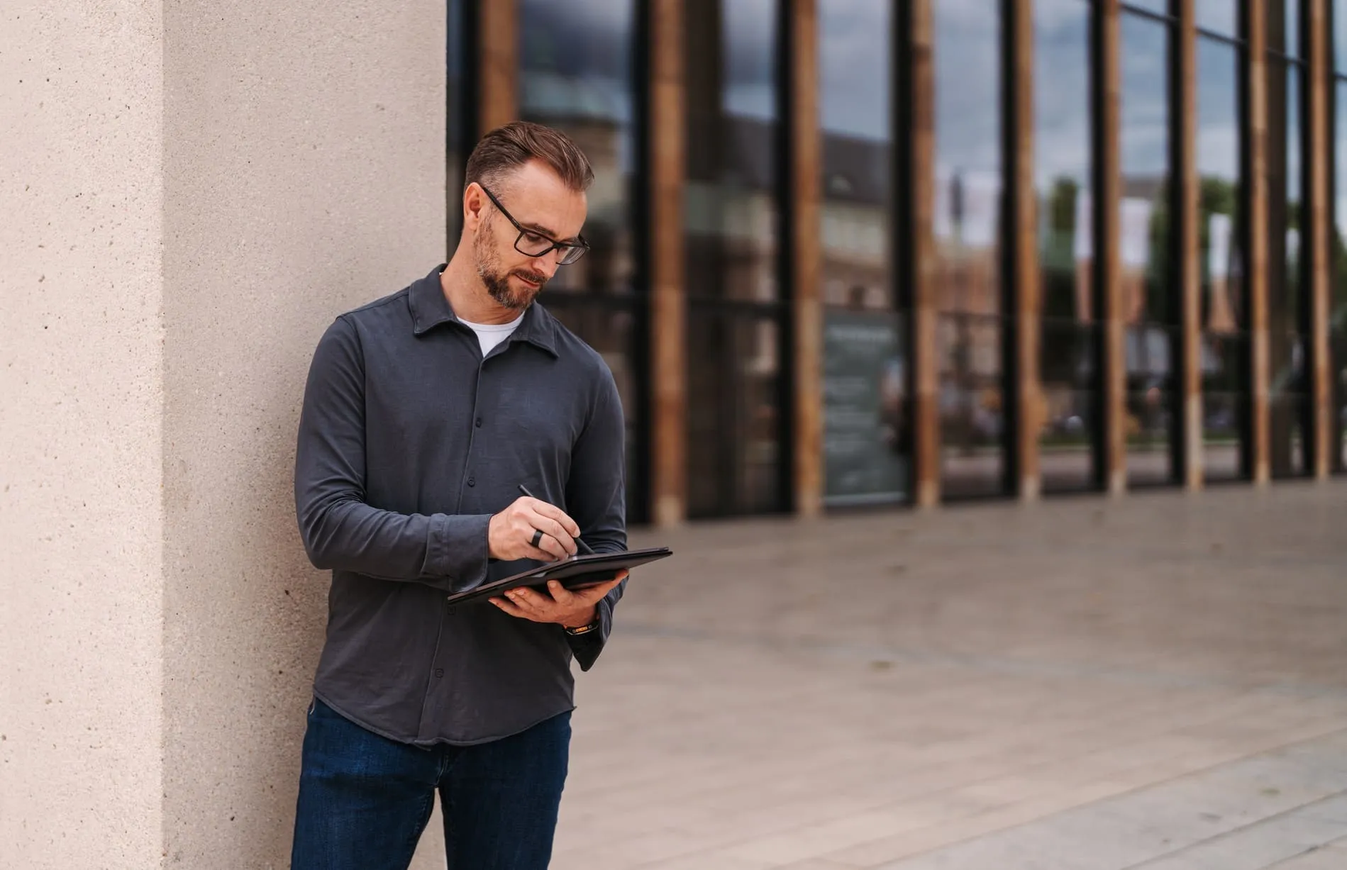Patrick Lenz macht konzentriert Notizen auf seinem Tablet vor einer Hauswand – das Warum hinter Entscheidungen festhalten für Mitarbeiter und KI