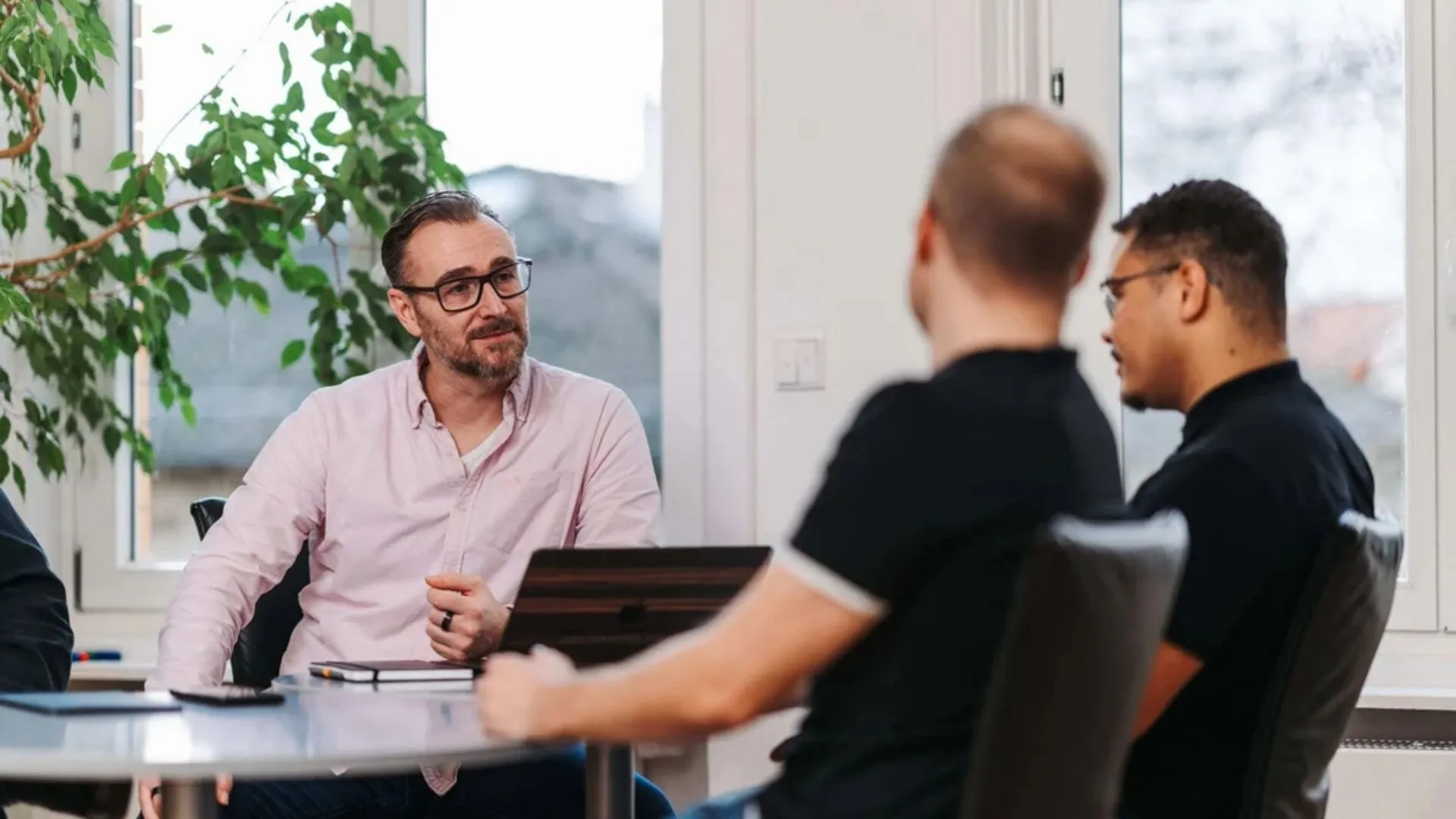 Patrick Lenz im Gespräch mit zwei Kollegen an einem Besprechungstisch