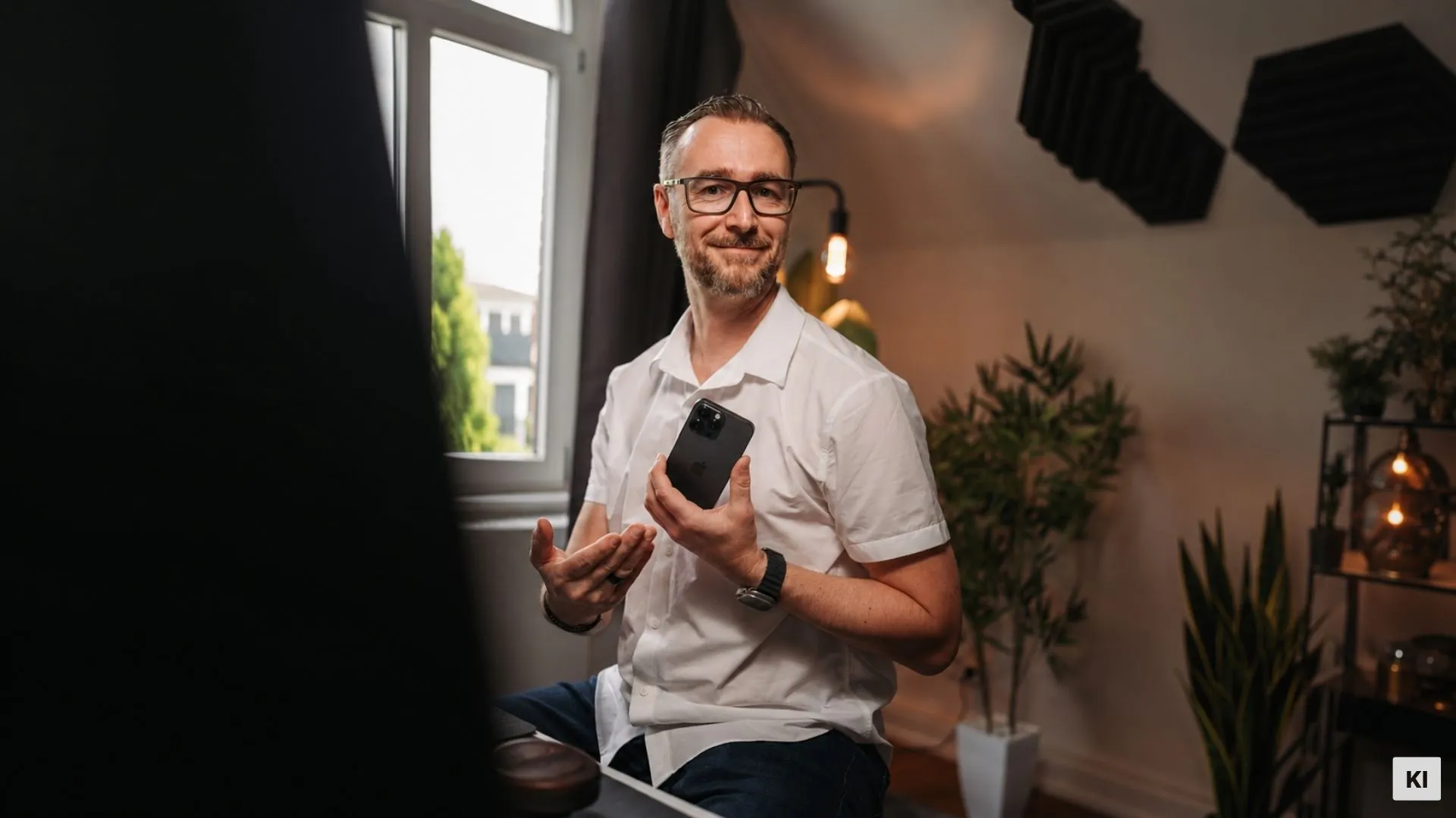 Patrick Lenz schaut in die Kamera und hält ein Handy in der Hand