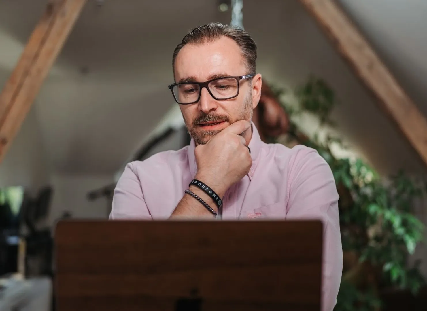Patrick Lenz sitzt nachdenklich mit der Hand am Kinn vor seinem Laptop in einem Dachgeschossbüro