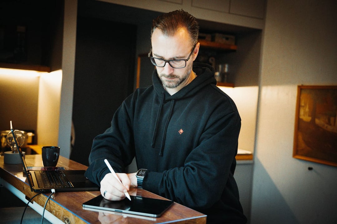 Patrick Lenz konzentriert beim Skizzieren auf dem iPad mit Laptop und Kaffee – Vorarbeit für ein eigenes Pflichtenheft vor jeder Systemoptimierung