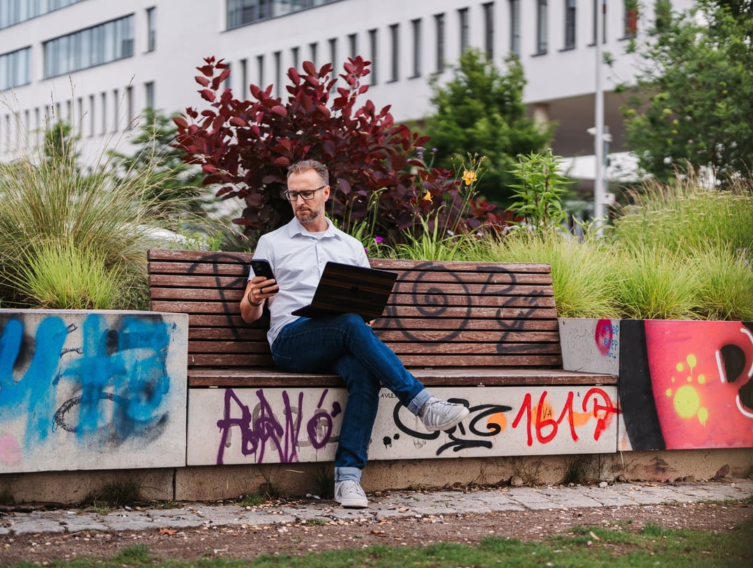 Patrick Lenz draußen mit Handy und Laptop